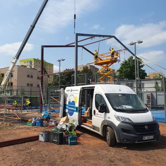 Stawianie konstrukcji hali do padla - prace z użyciem dźwigu i podnośnika